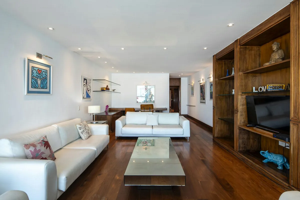 Living room of the Copacabana duplex penthouse with white sofas, a glass coffee table and wooden shelves