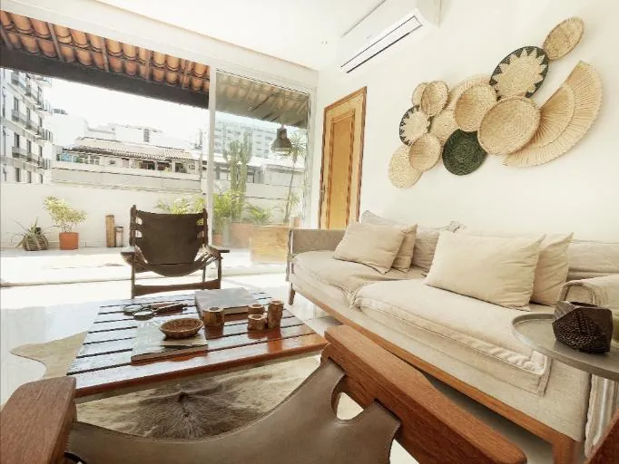 Living room of an Ipanema penthouse with linen sofas, woven wall baskets and doors open to a terrace
