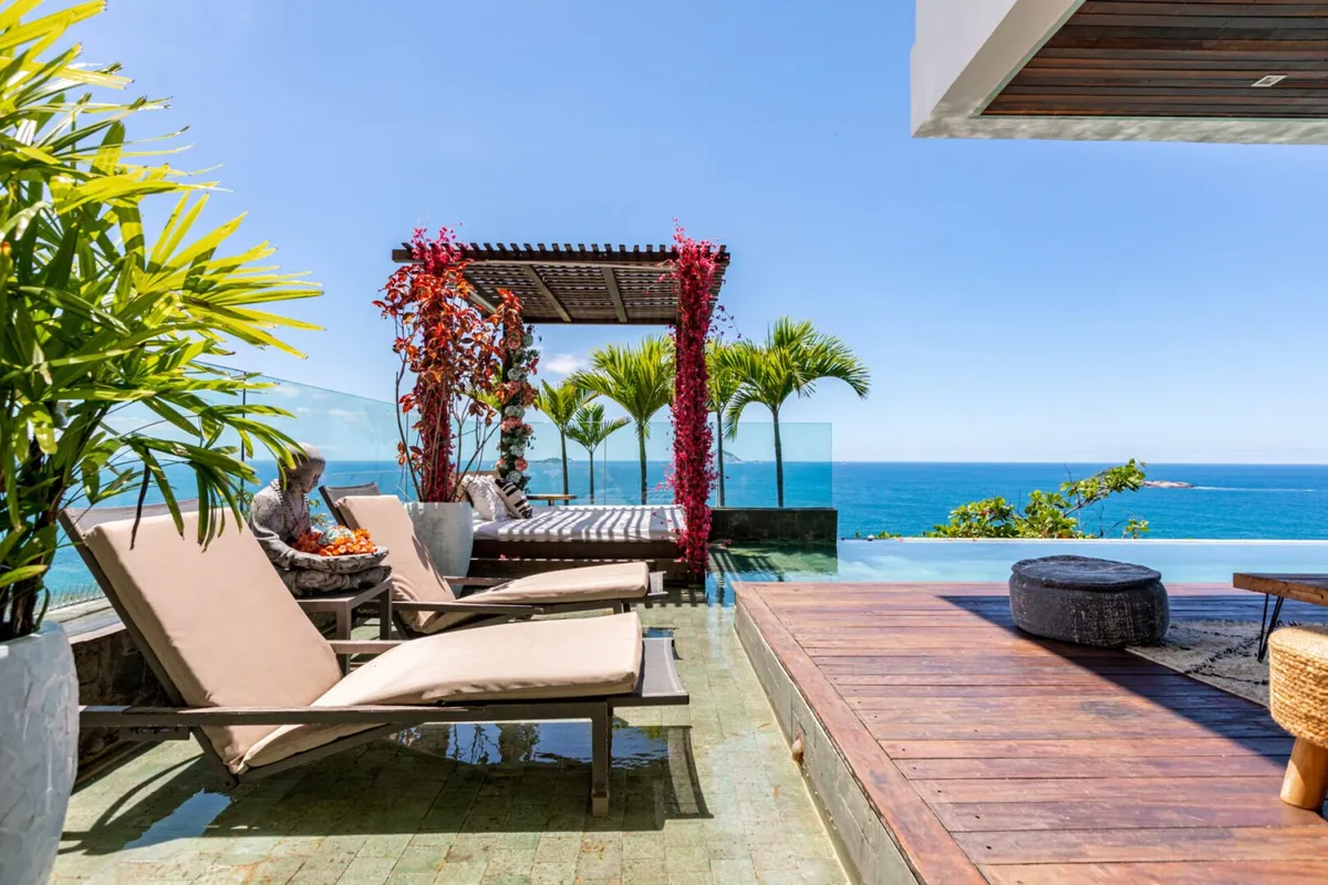 Loungers and a red pergola on the deck of a Joá villa above the ocean