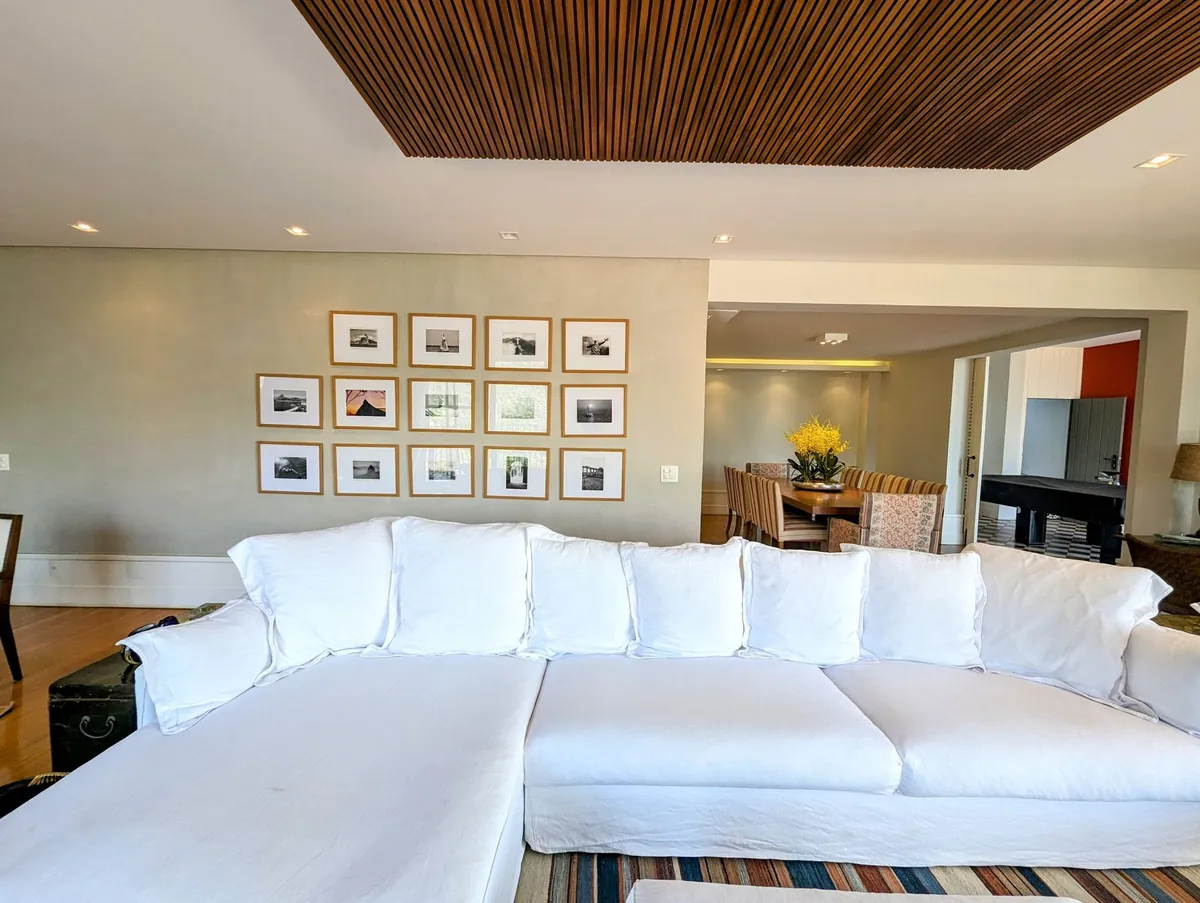Living room of a Santa Teresa house with a large white sofa, framed photographs and a timber ceiling