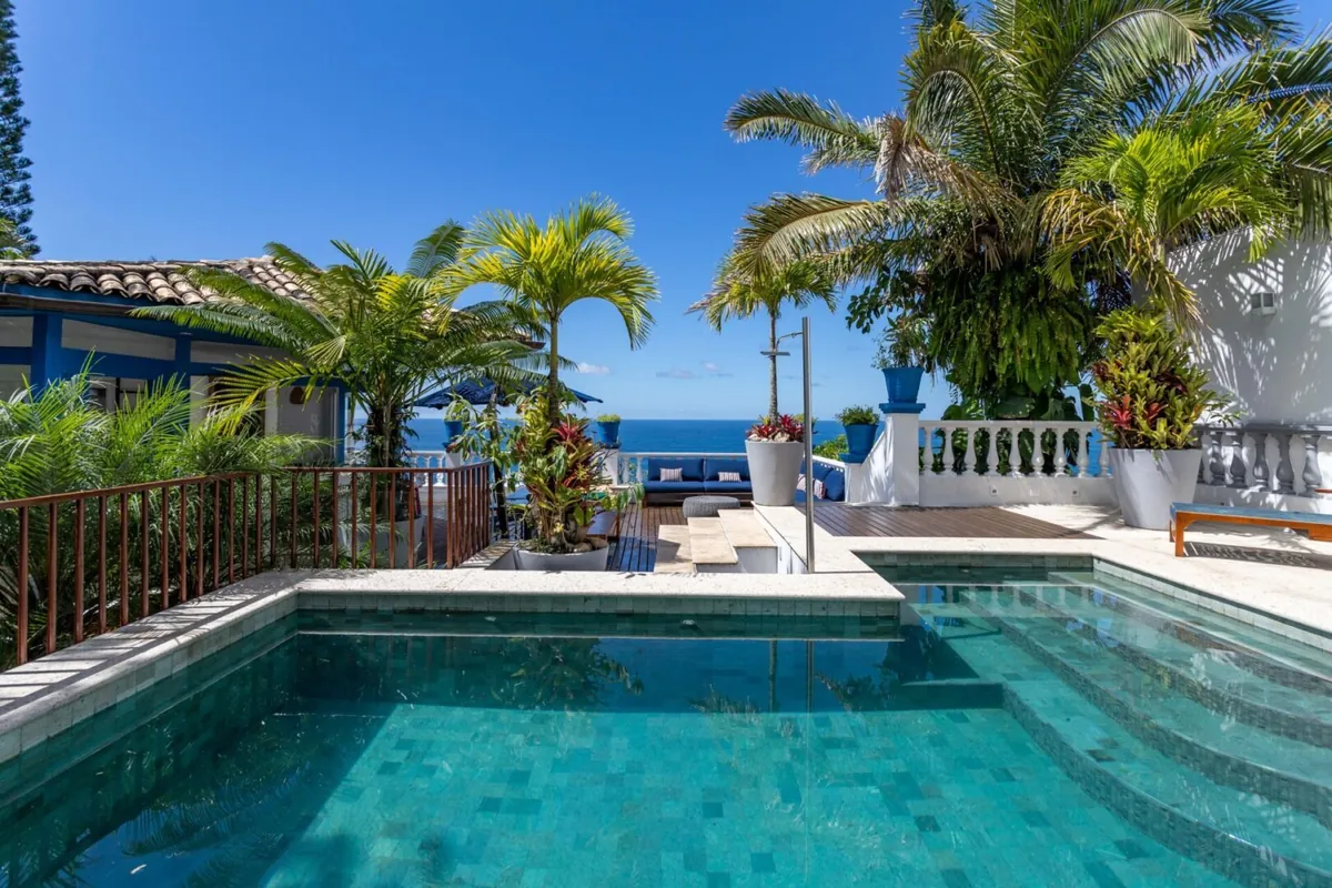 Green-tiled pool of the Elis Regina House in São Conrado with palms, a white sculpture and the ocean beyond