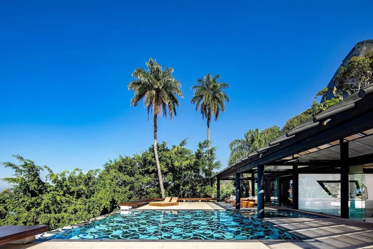 Two tall palms above the pool of the São Conrado Beach View Villa with the mountain and the glass pavilion