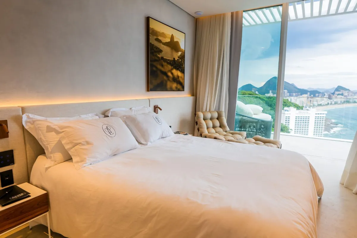 Bedroom of the Vidigal duplex penthouse with a large bed, warm lighting and a window view of Leblon and Ipanema
