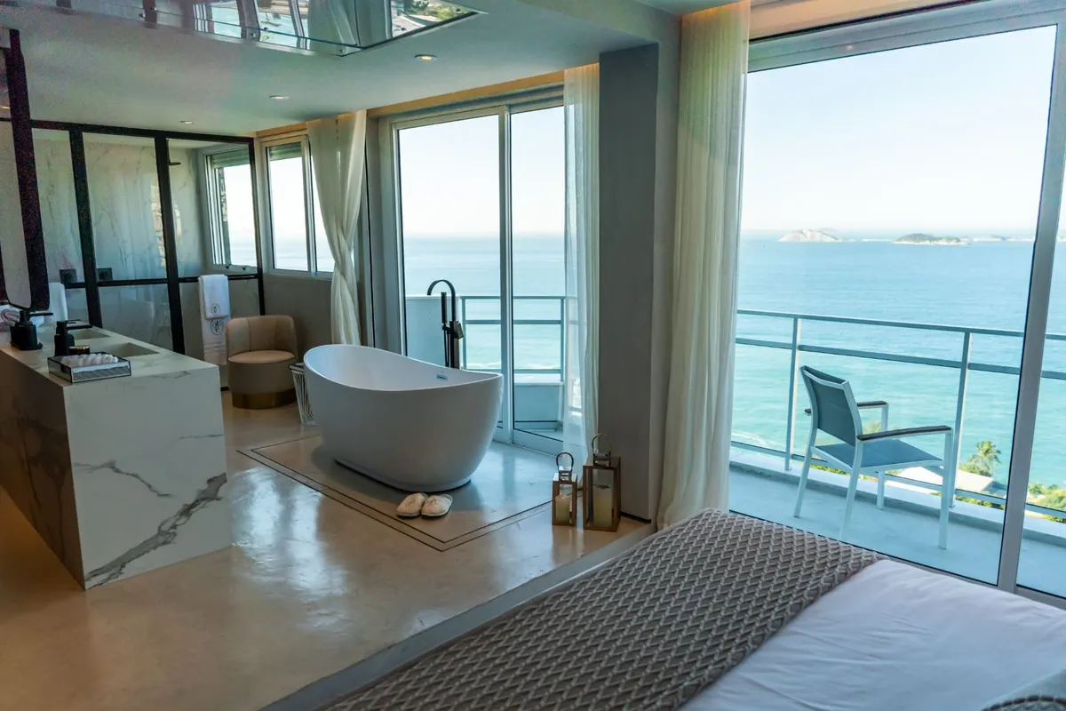 Suite of the Vidigal duplex penthouse with a freestanding bathtub by the window and the sea beyond the balcony