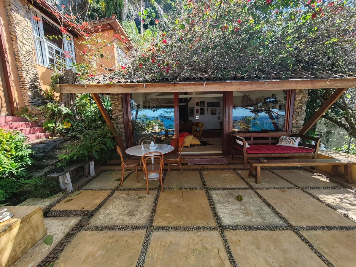 Garden pavilion of a Vidigal house with a tiled roof covered in plants, a stone courtyard and tropical trees